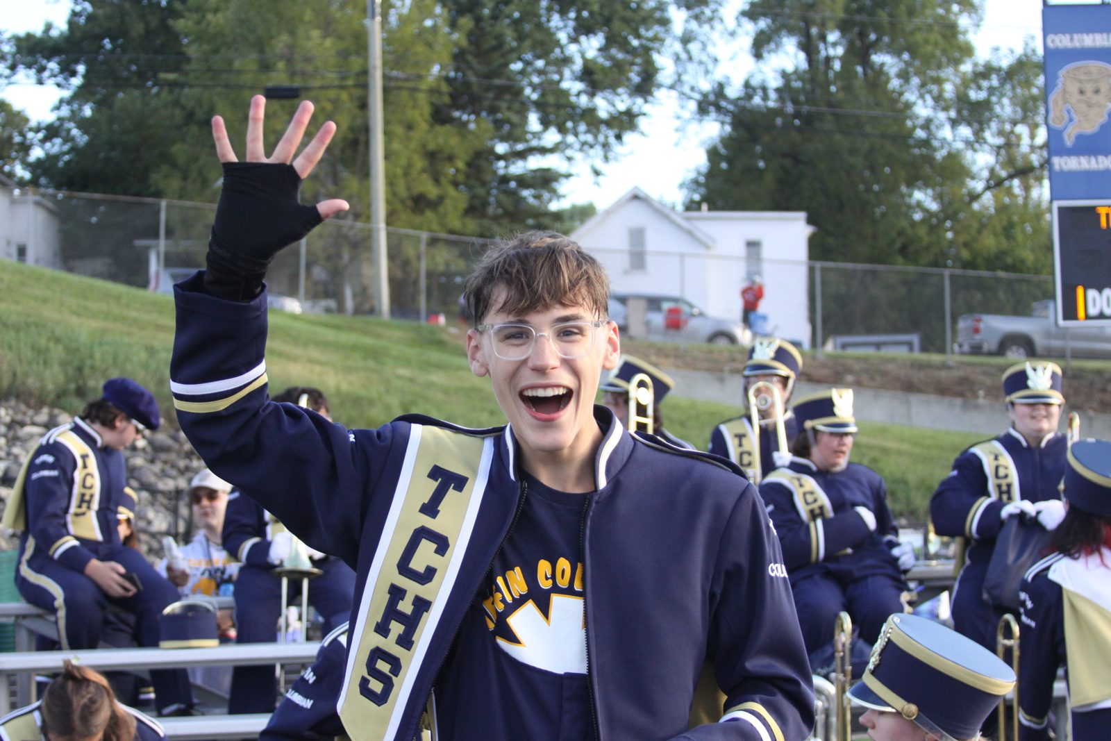 A smiling Columbian band member in uniform waves at the camera from the stands.