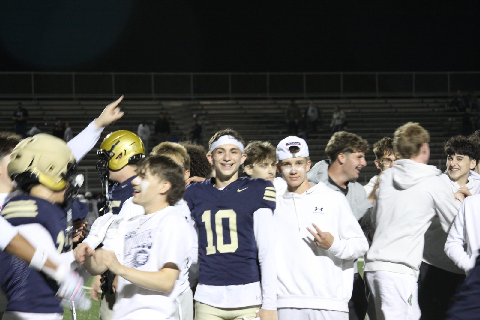 Smiling Columbian football players and students gather on the field at night.