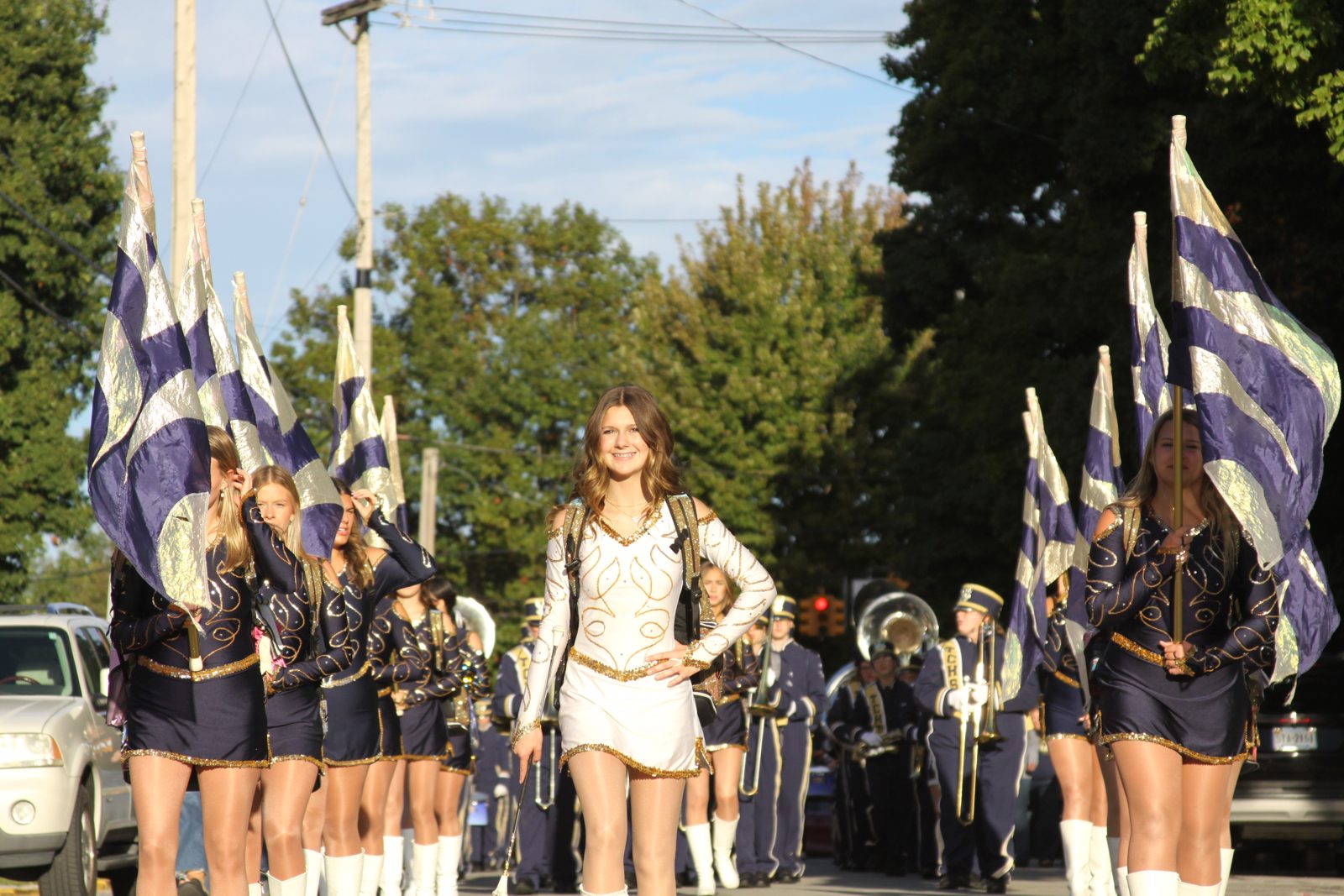 A Columbian band leader in a white uniform smiles while marching ahead of flag carriers and the band during a parade.