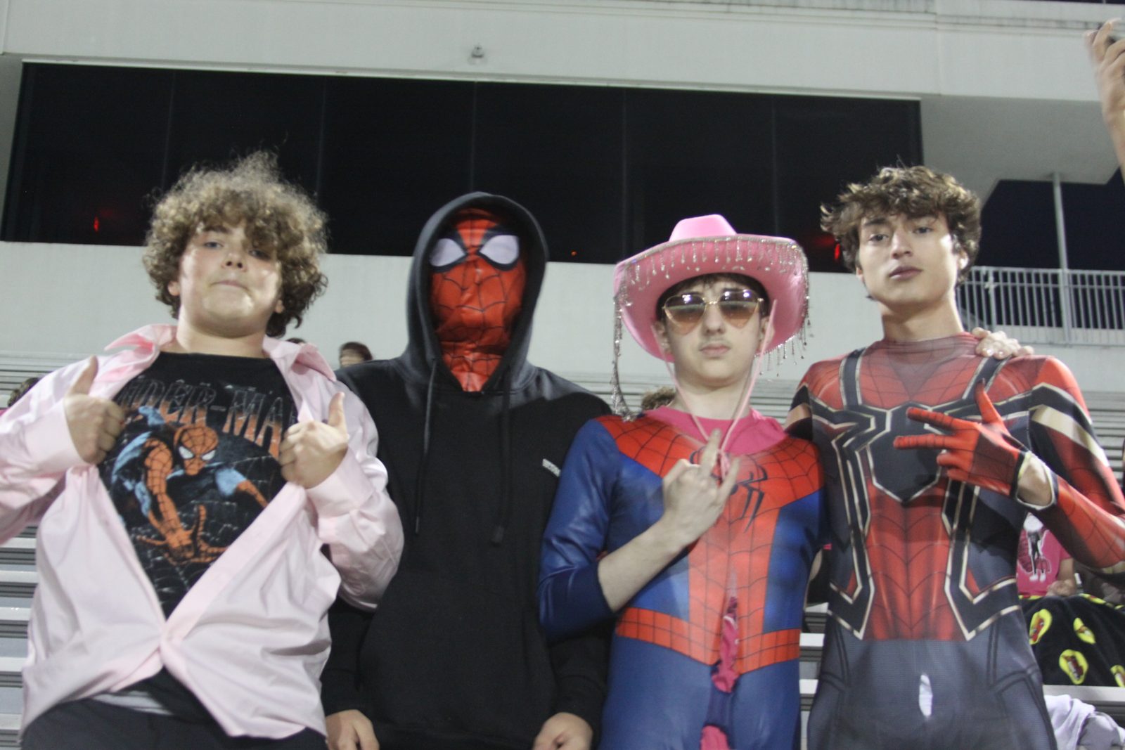Four Columbian students in Spider-Man costumes and pink accessories pose in the bleachers.