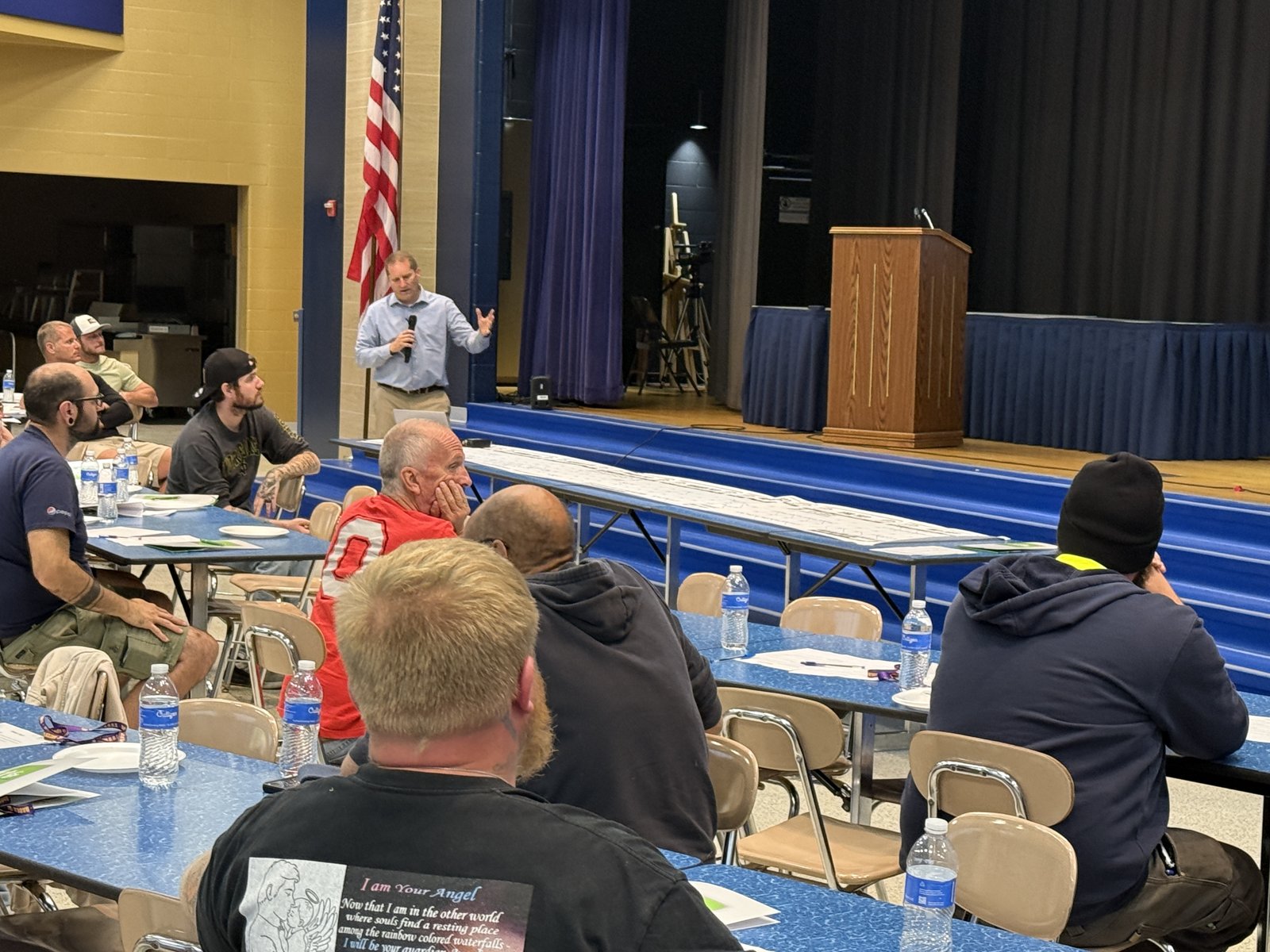 Noble Principal Mike Newlove speaks to volunteers seated at cafeteria tables during the WATCH D.O.G.S. kickoff.